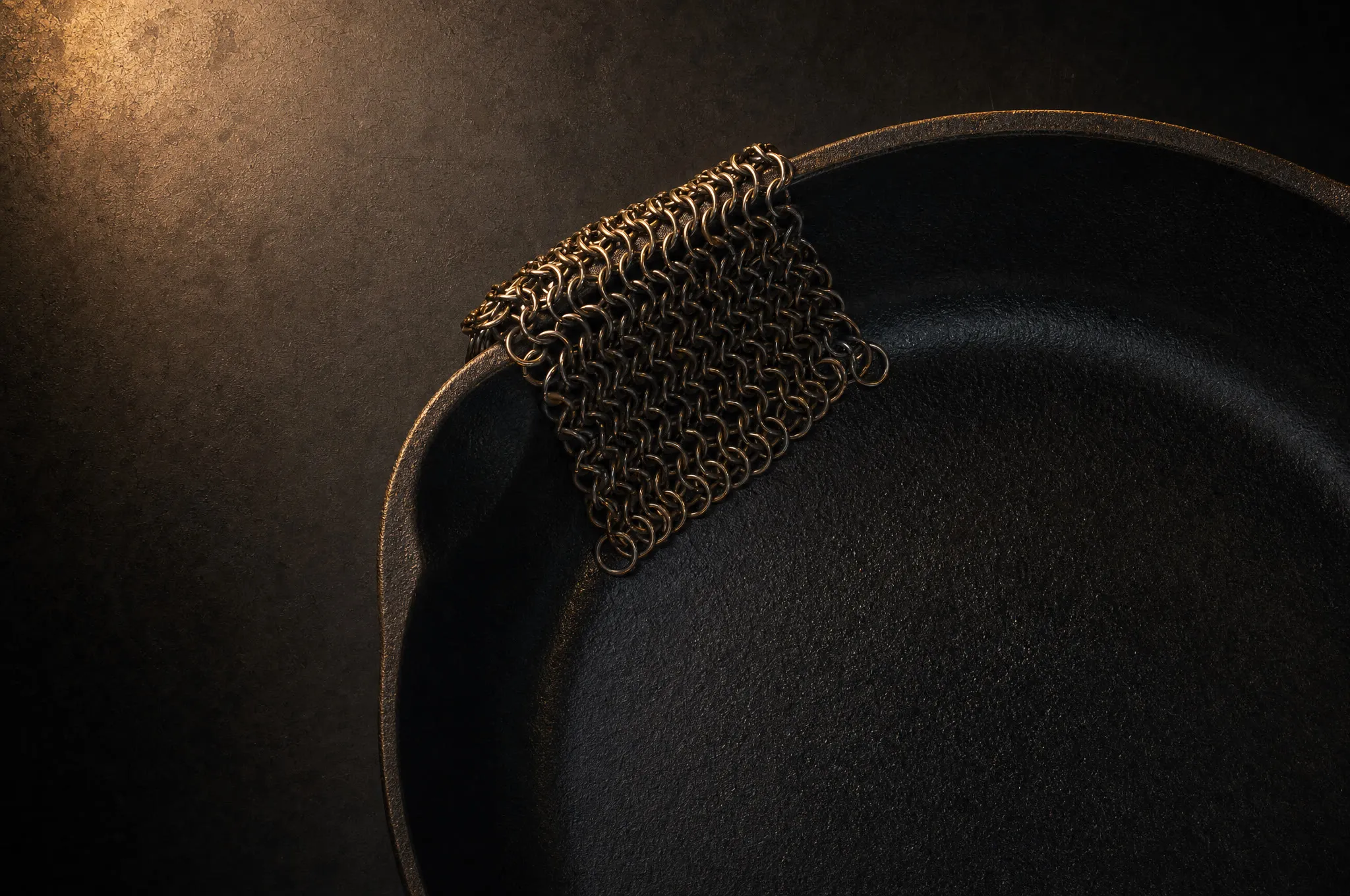 Chainmail scrubber draped over the rim of a cast iron skillet